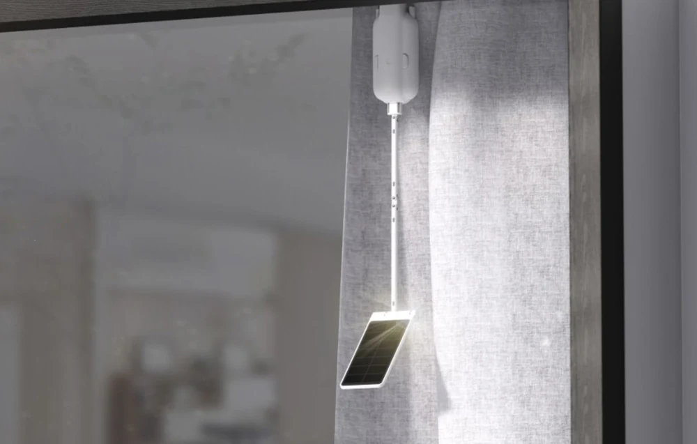 SwitchBot solar panel hanging beside a curtain in sunlight