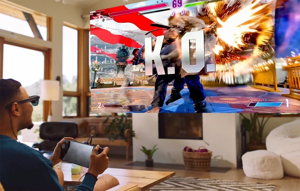 Vyras su XR akiniais žaidžia kovos žaidimą nešiojamoje konsolėje, matomoje dideliame ekrane
