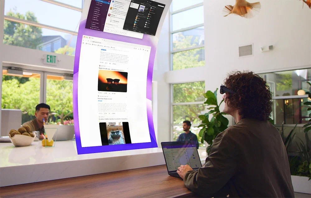 Žmogus su XR akiniais dirba prie nešiojamojo kompiuterio, žiūrėdamas virtualius dokumentus ir sąsajas biuro erdvėje