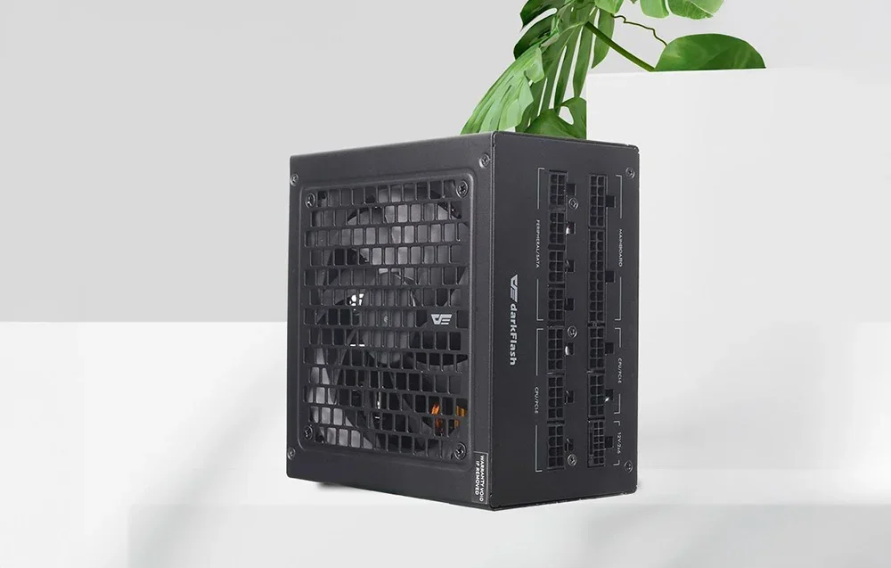 Juodas DarkFlash maitinimo blokas ant balto stalviršio su žaliu augalu fone