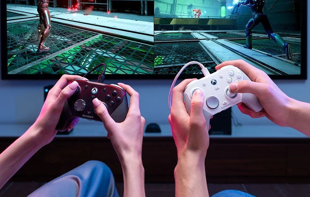 Dviejų žmonių rankų stambus planas su GameSir valdikliais žaidžiant per televizorių.