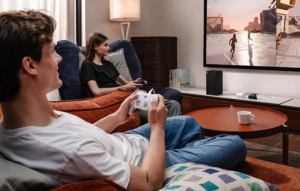 Du žmonės žaidžia per televizorių naudodami GameSir valdiklius, vienas baltas, kitas juodas.