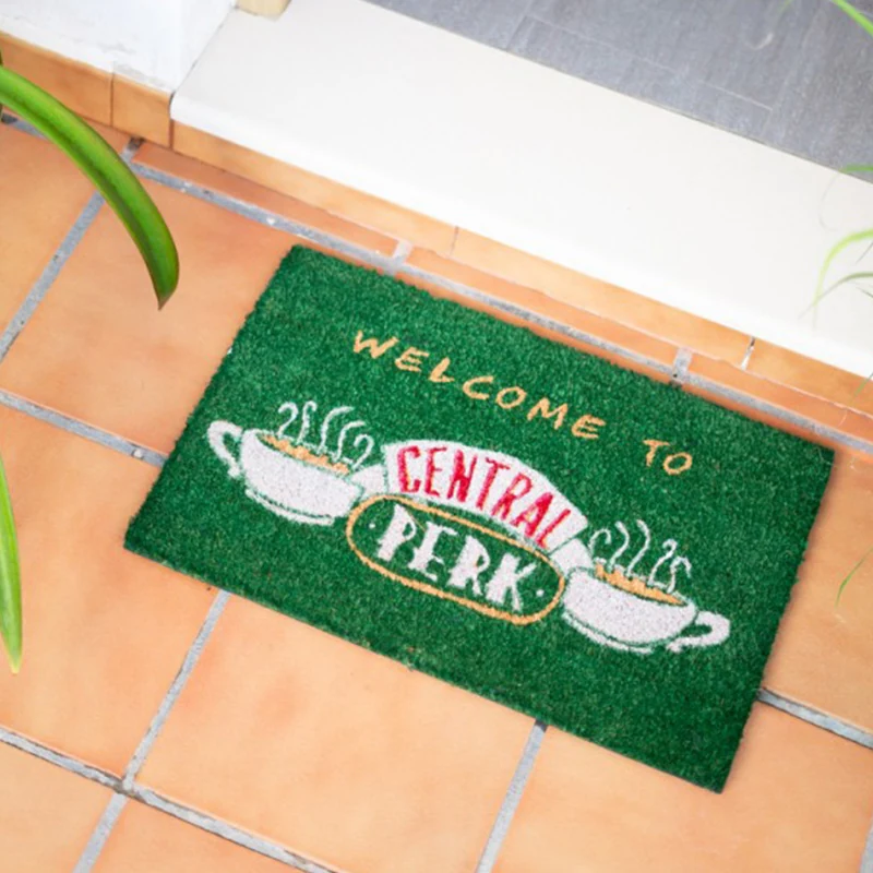 Žalias „Central Perk“ durų kilimėlis prie durų ant plytelėmis išklotų grindų