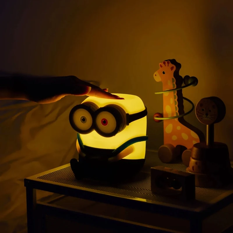 Ranka liečia šviečiančio „Minions“ Bobo šviestuvo viršų prie lovos